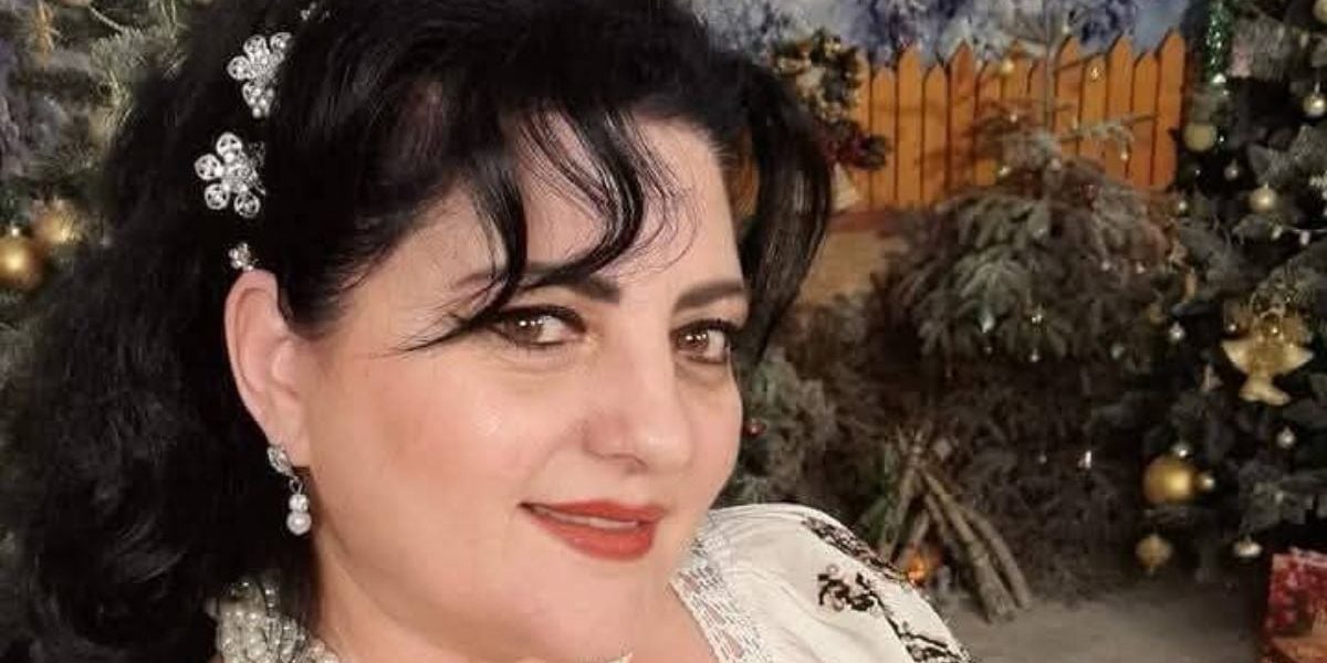 Imagine de prim plan cu Mihaela Cojocaru, cu o bentiță cu flori în păr, iar pe fundal un decor de Crăciun