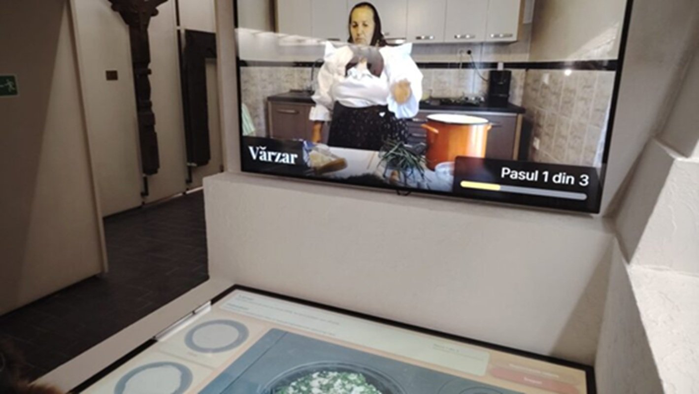 Gătit virtual la Muzeul Etnografic Sighetu Marmației: vizitatori, ghidați de socăcițe, folosesc un ecran touch